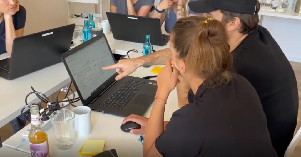zwei Mitarbeitende sitzen gemeinsam an einem Laptop und zeigen auf den Bildschirm